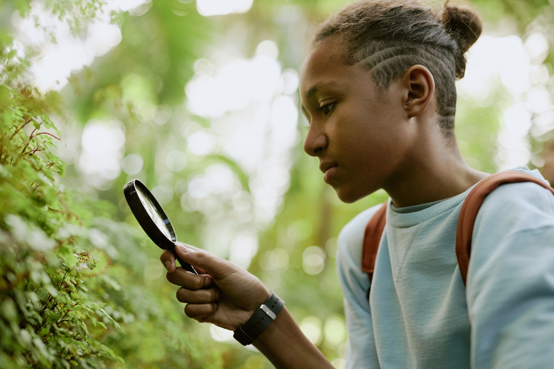 Black Teenager Looking Closer At Plants In Botanical Garden